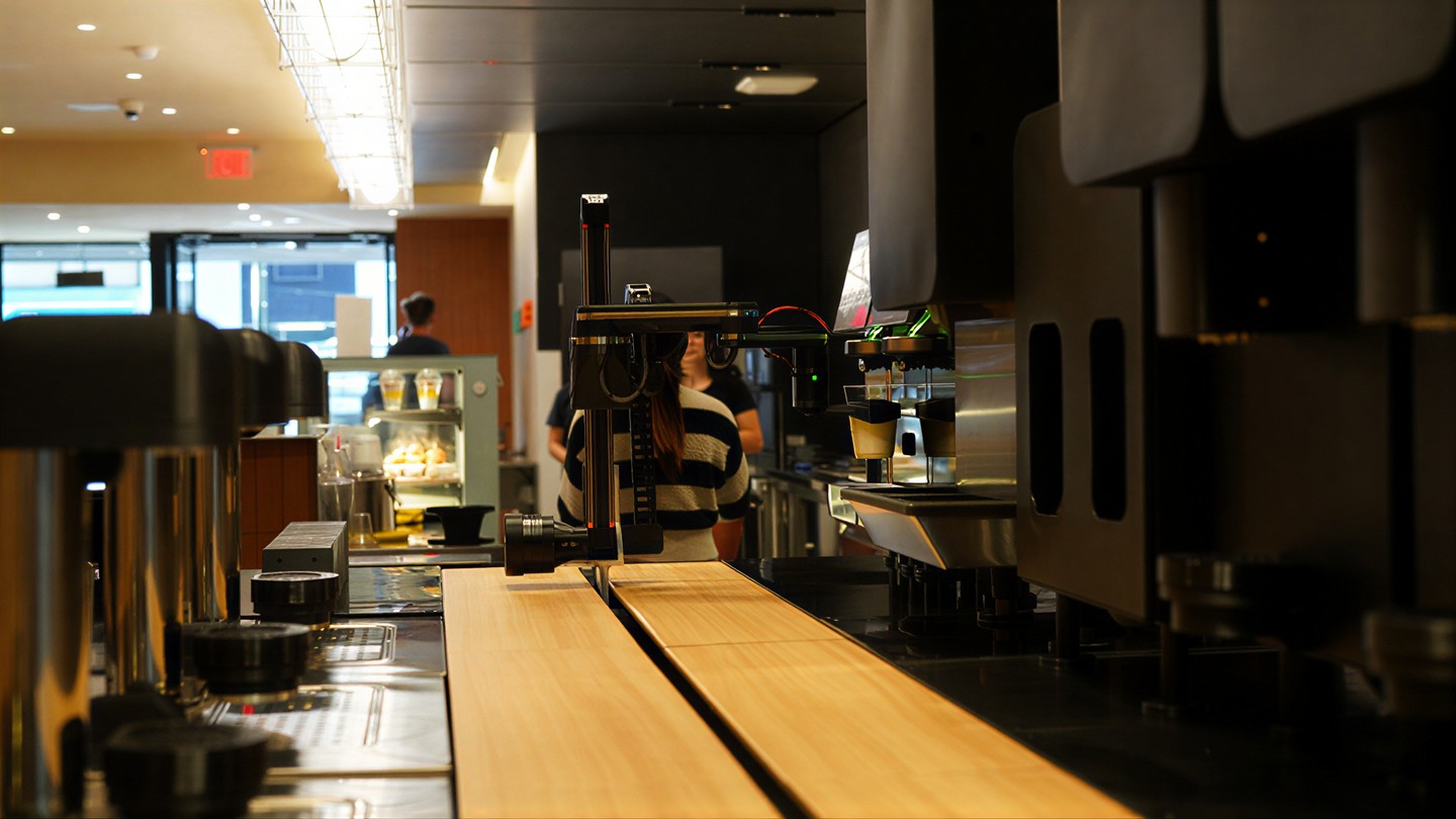 Gantry arm working the bar: machine column, camera head and the service counter